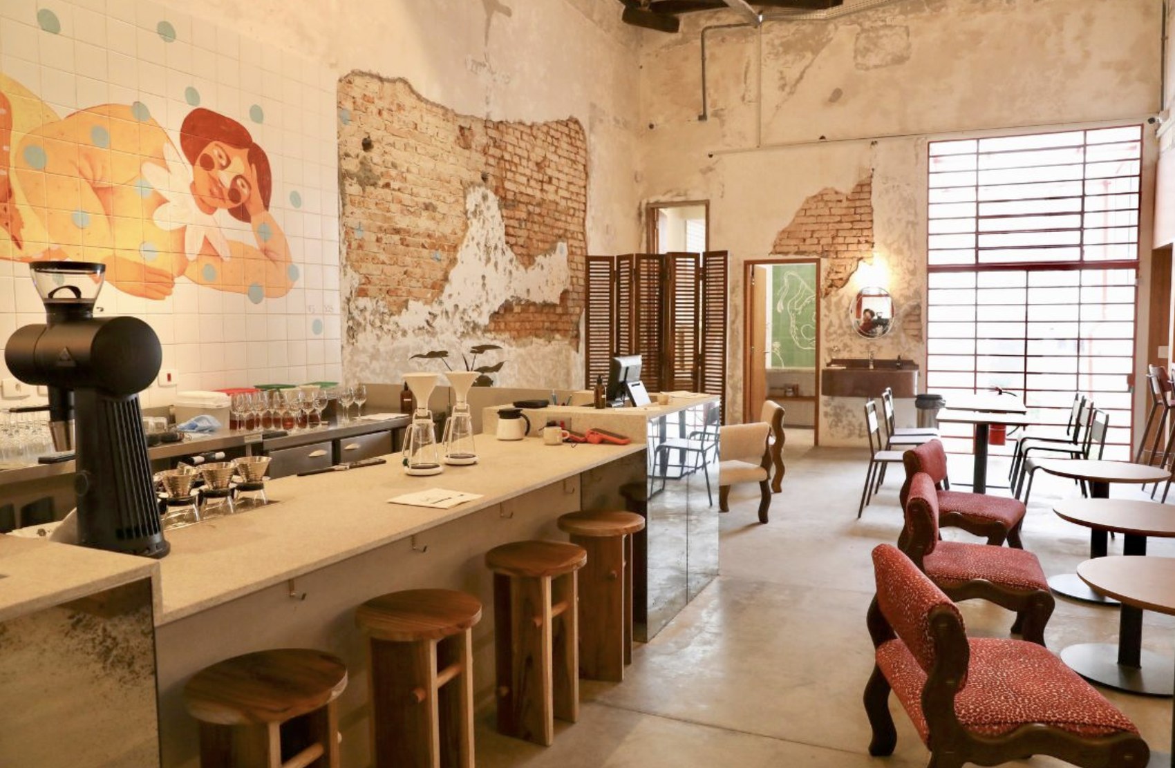 The dining room at Cafetina, with a tiled mural, exposed brick and red upholstered chairs
